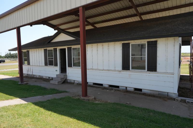 A weathered single-story house with a covered porch and green grass in front.