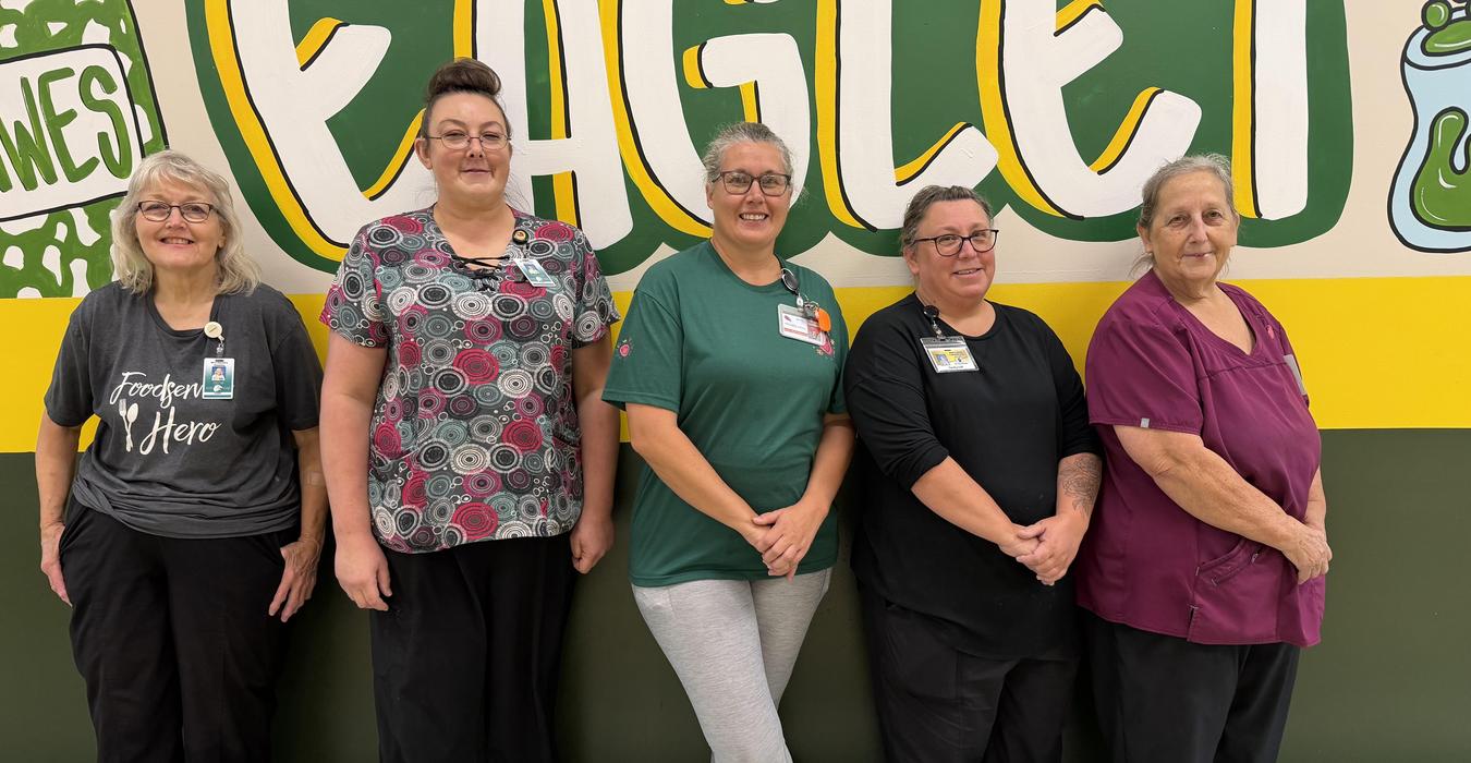 Five women standing in front of a colorful mural with the word 'Eagle'.