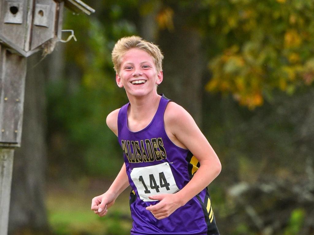 A cross country athlete smiling while he runs during a meet.