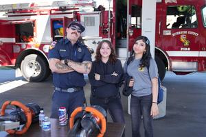 firefighter and two students pose in front of fire truck
