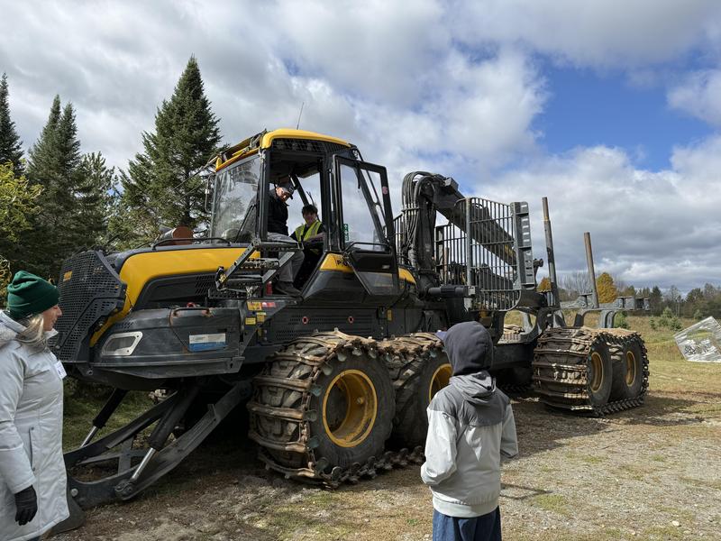 A large machinery vehicle with children observing it in an outdoor setting.