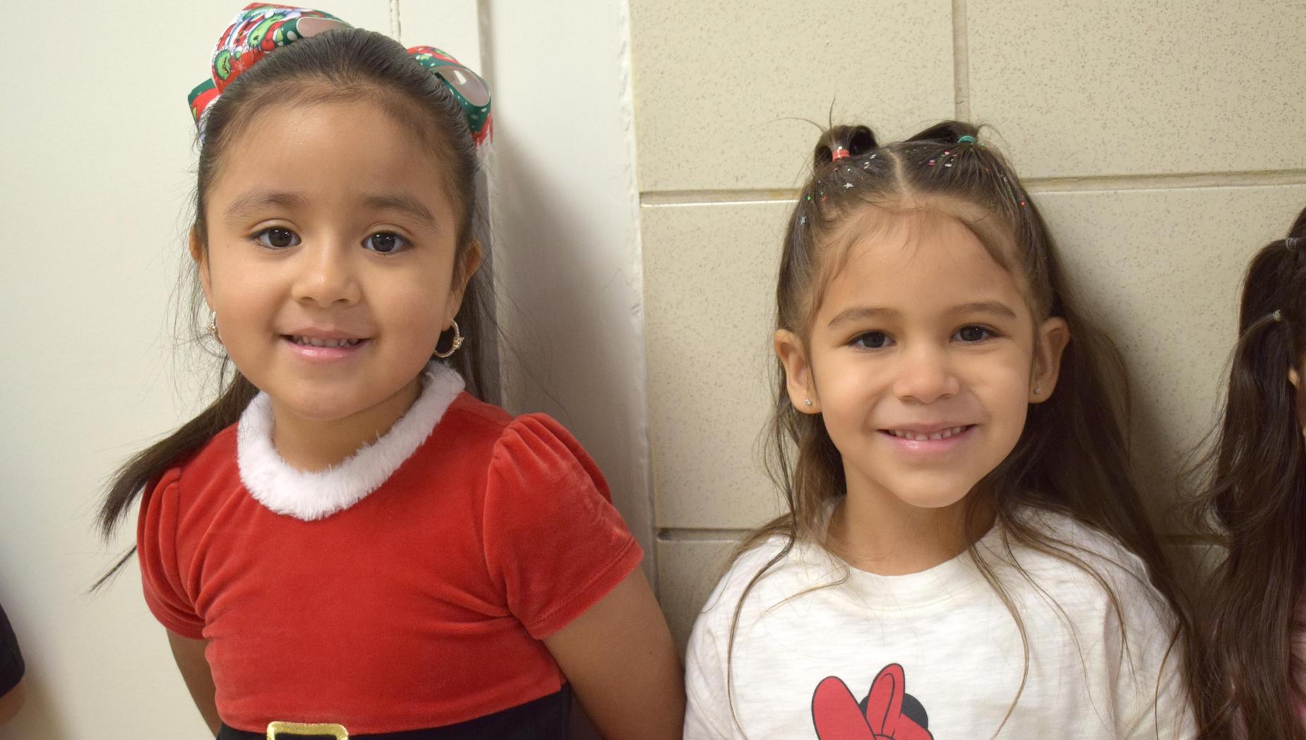 Two young girls smiling together, one in a red Christmas dress and the other in a white shirt.
