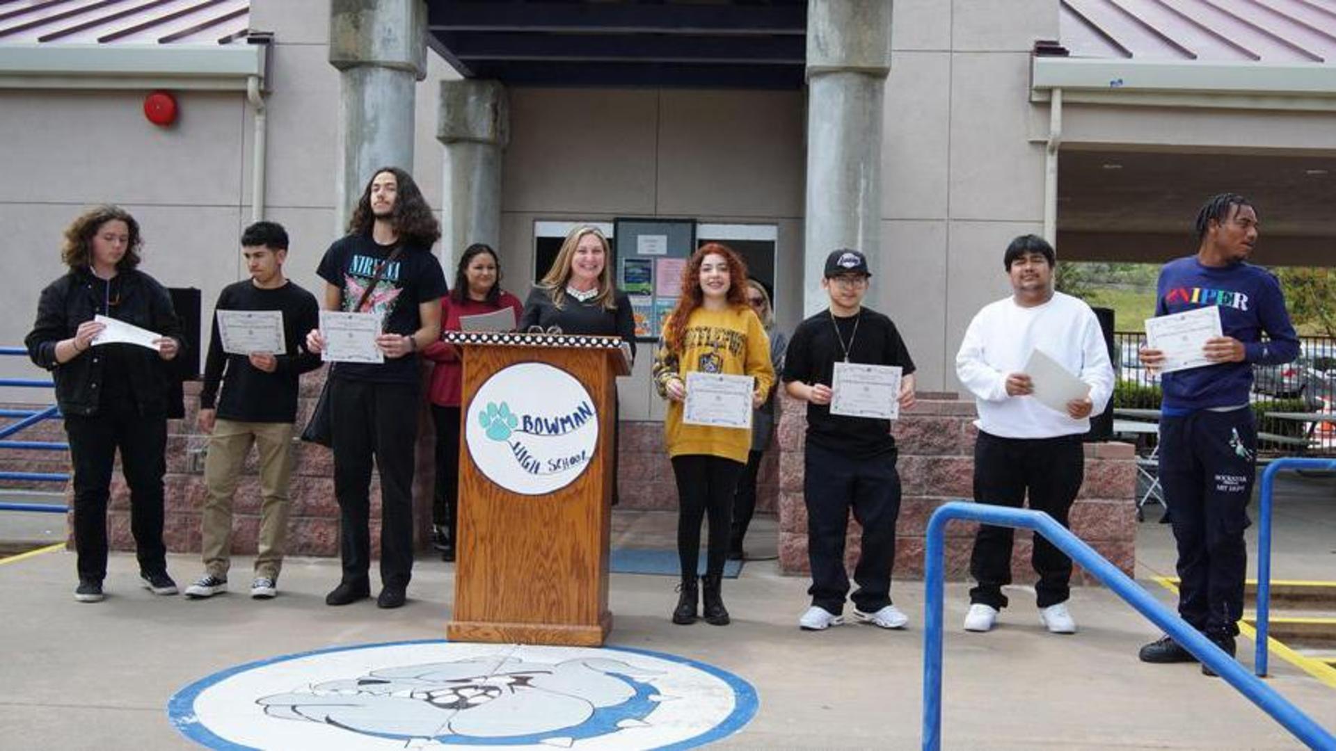 Bowman Principal Nina Zamora and students pose with certificates of graduation in the school outdoor quad.