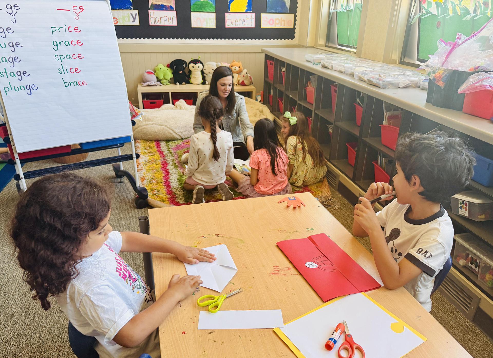 Image with teacher with students at carpet and other students at the table