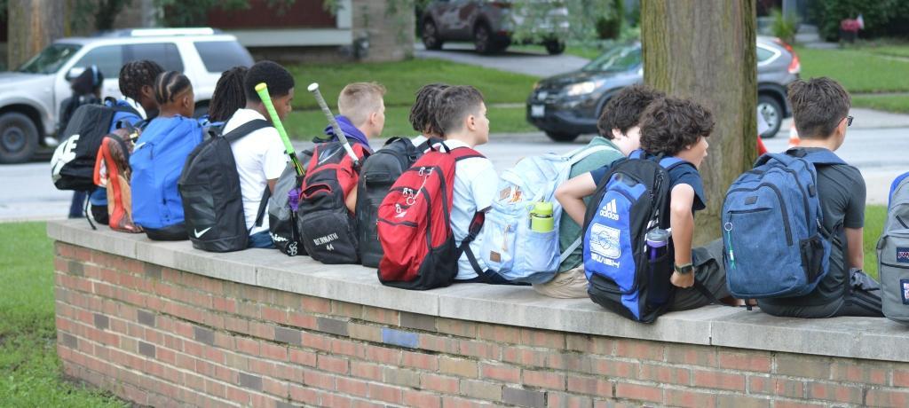 Students with backpacks sit on entrance wall.