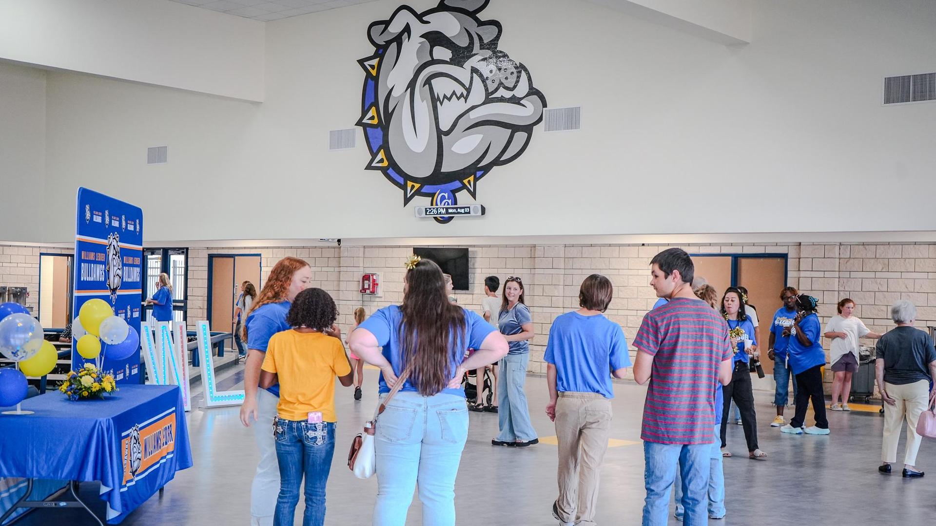 People gather in a school lobby decorated with a bulldog icon.
