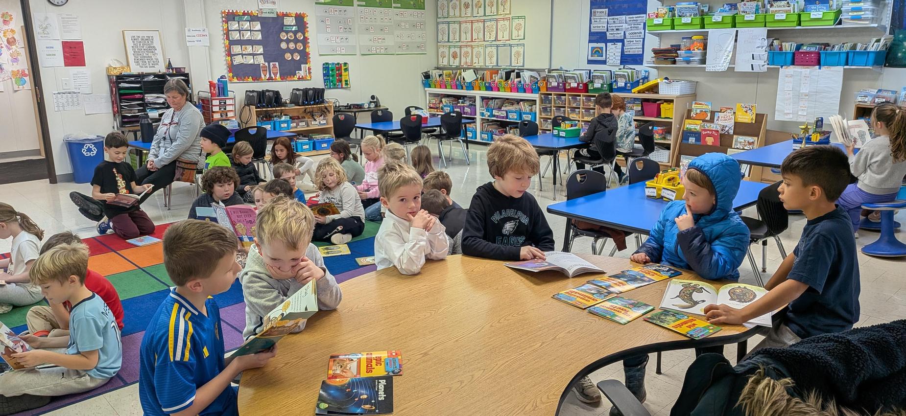 A classroom scene with children reading and engaged in group activities around tables.