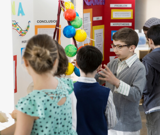 Four elementary students standing around Science Fair posters and discussing projects