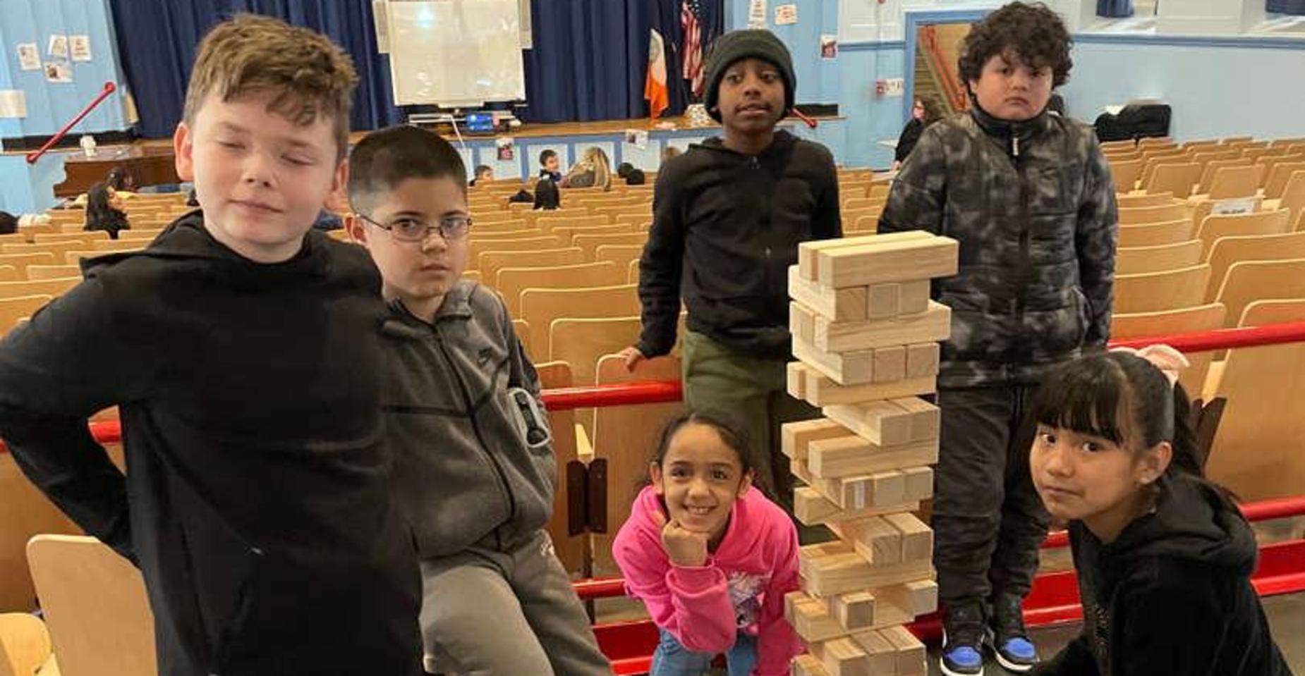 Children posing next to a tall stack of wooden blocks in a hall.