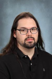 Serious man with long hair and glasses wearing a black shirt.