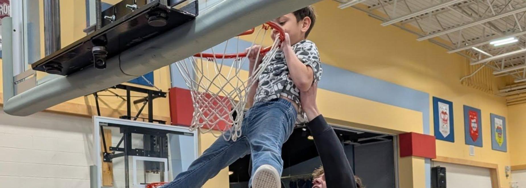 Students celebrate during a basketball event, with one being lifted by another.
