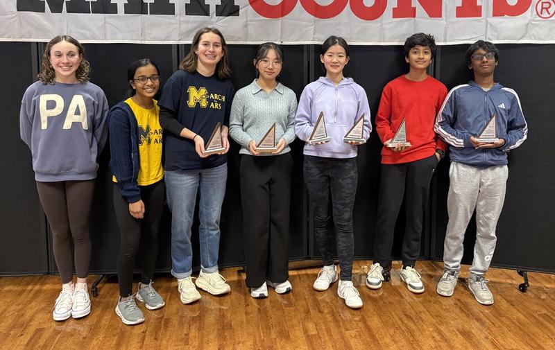 a group of seven students, some holding triangular trophies.