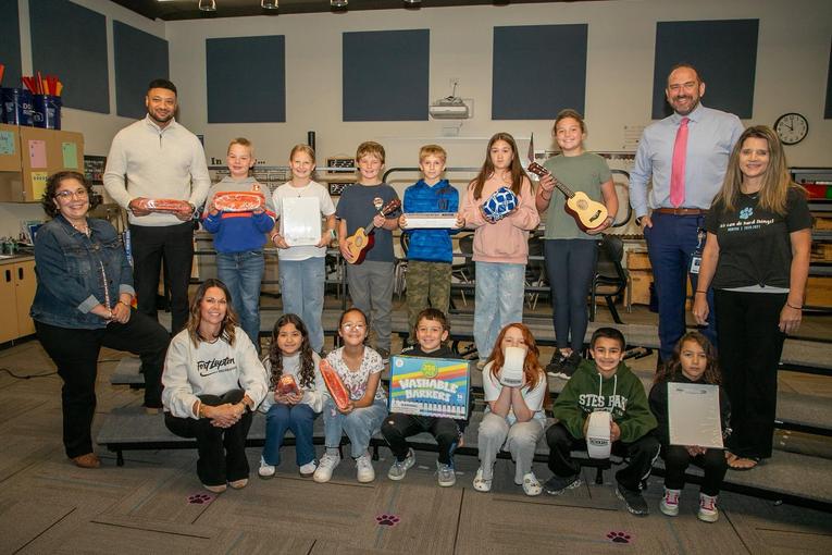 A group of children and adults holding various items in a classroom setting.