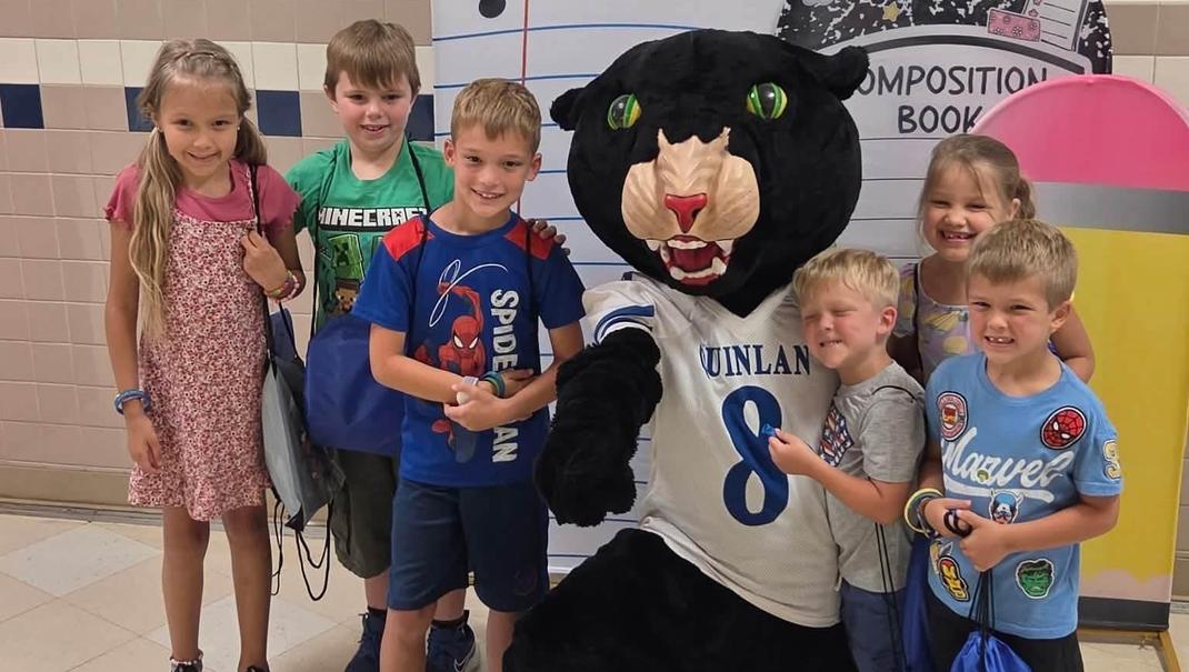 Children posing with a mascot in a school setting.