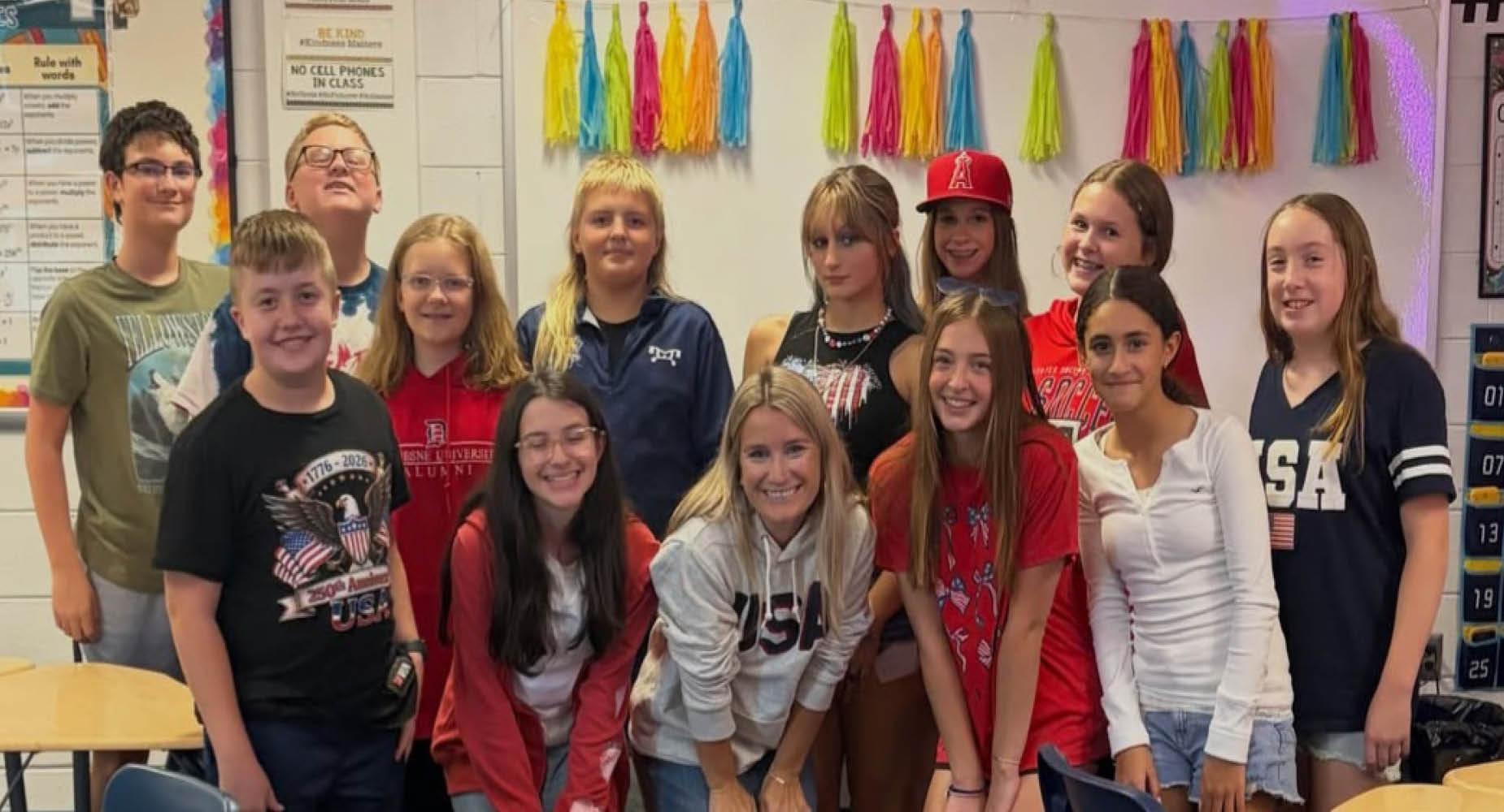 A group of twelve smiling students poses together in a classroom with colorful decorations.