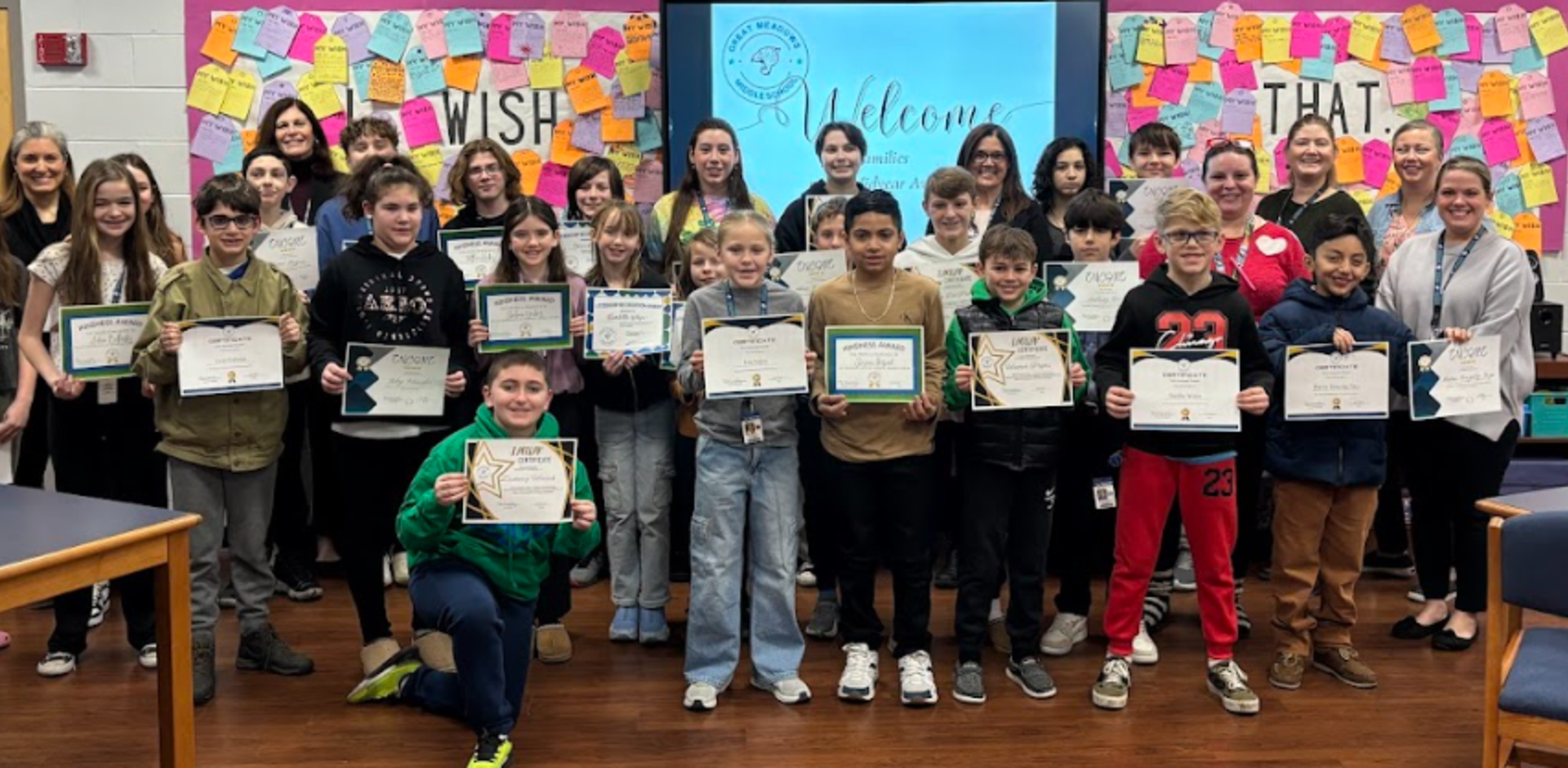 Group of students and teachers celebrating with certificates in a classroom setting.