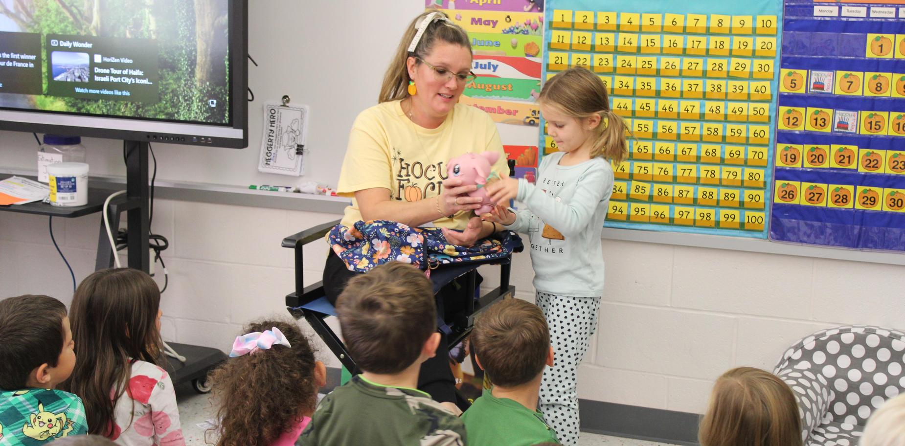 Teacher showing a stuffed animal to children sitting on the floor in a classroom.