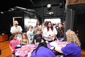 A crowd of people, mostly children, gathered around a table with crafts and activities.