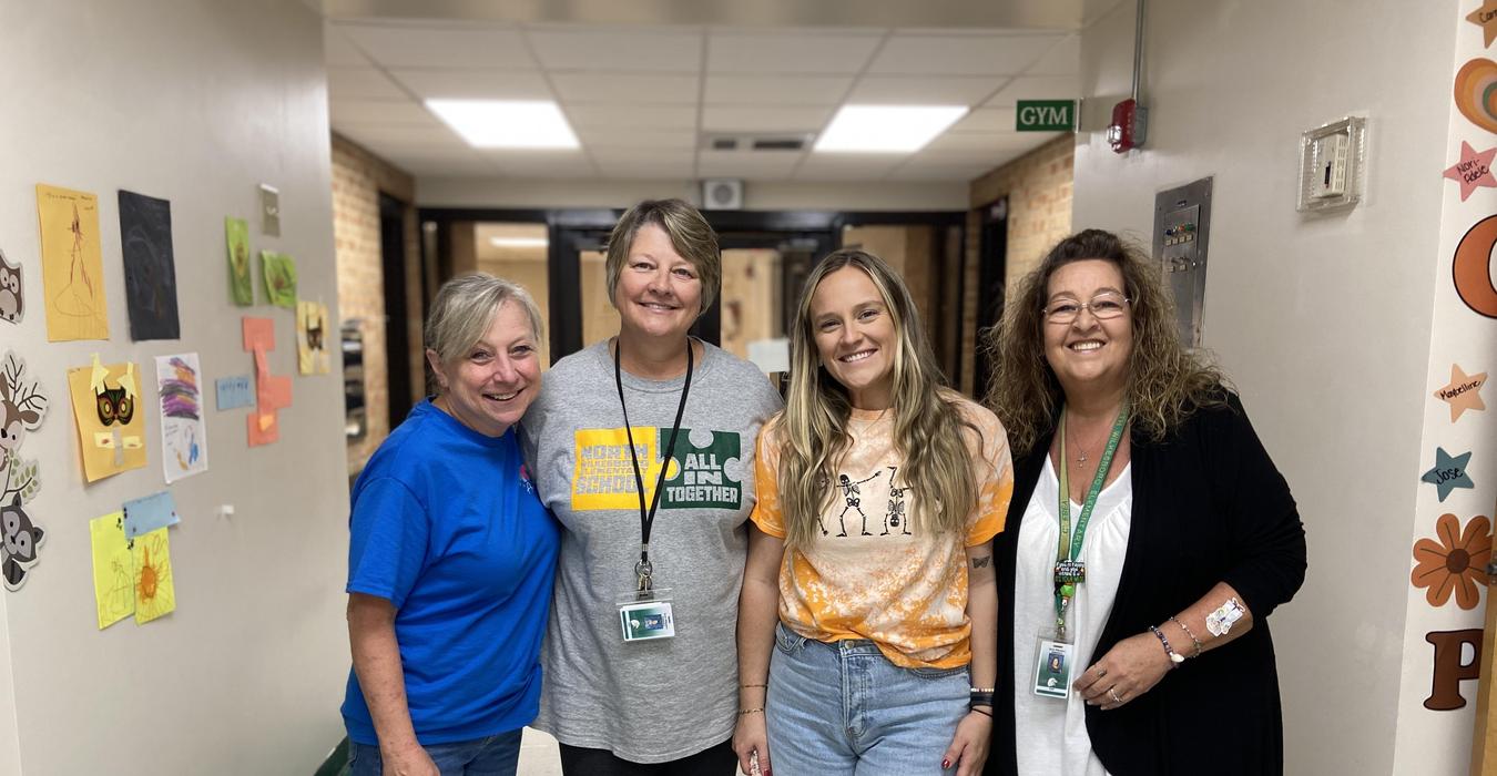 Four women posing in a school hallway, engaging with each other.