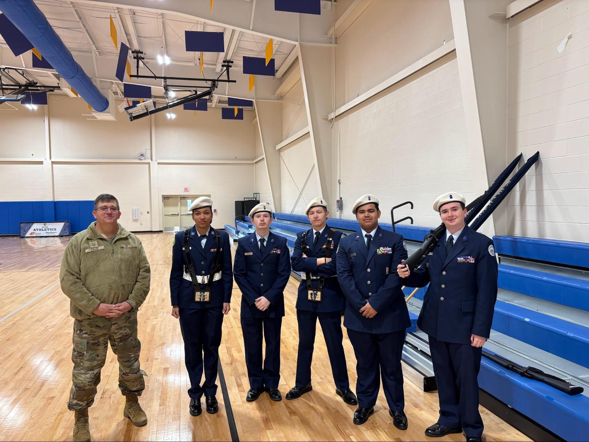 A military officer stands with cadets in uniforms inside a gym.