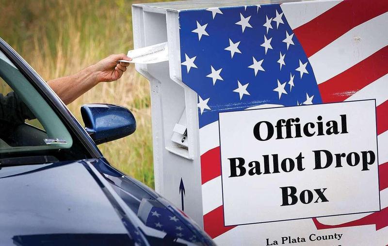 An adult in a vehicle reaches through the driver-side window to drop a ballot in a La Plata County Official Ballot Drop Box.