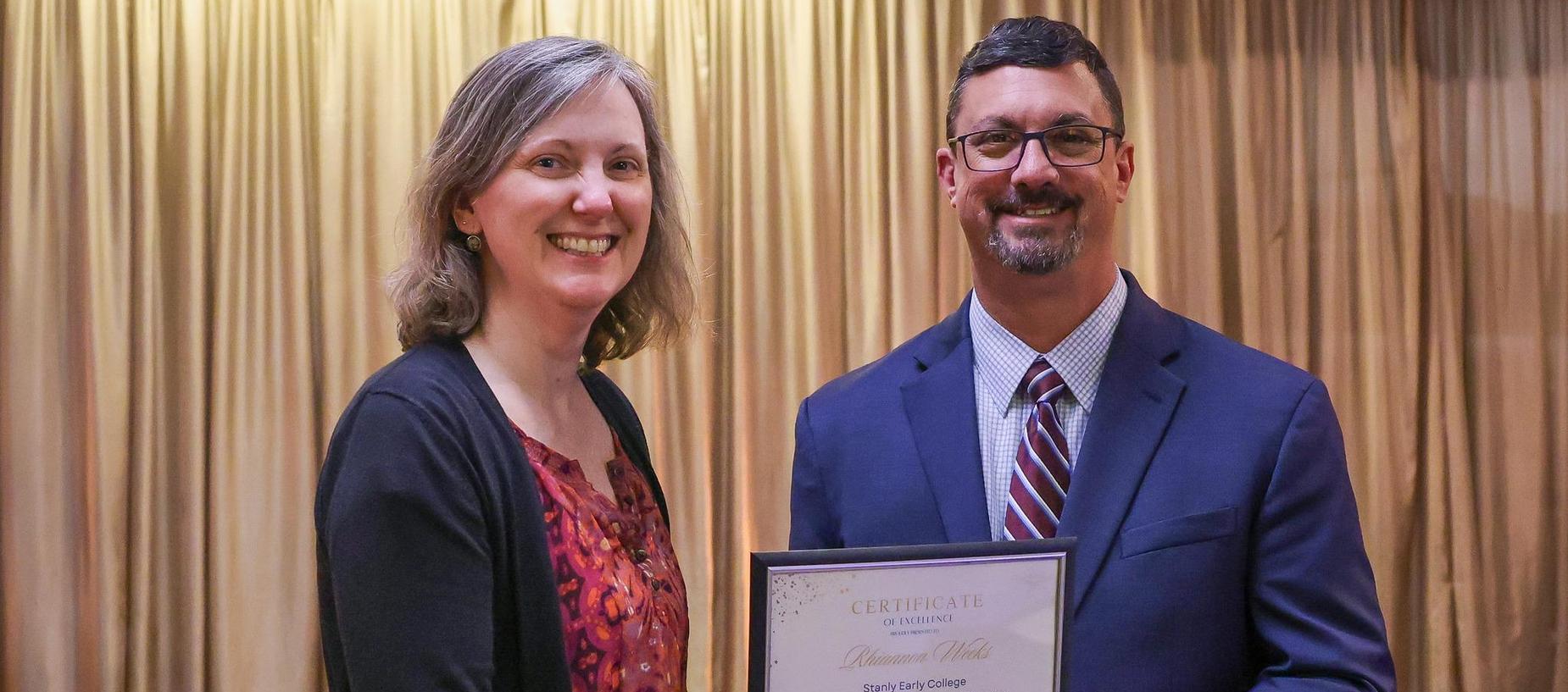 Two people smiling while holding a certificate during a ceremony.