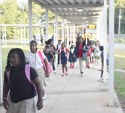 a group of students walking into the school building after getting off of the bus