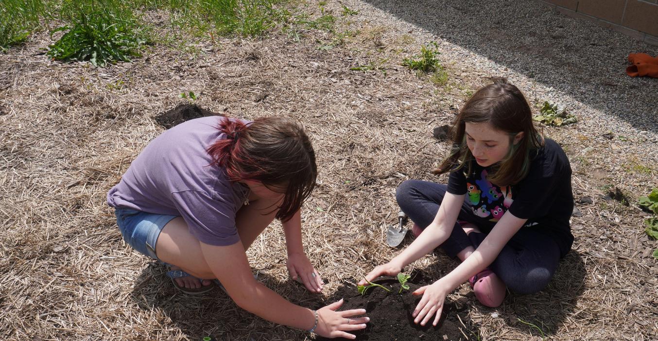 Two students plant seeds in the middle school garden.