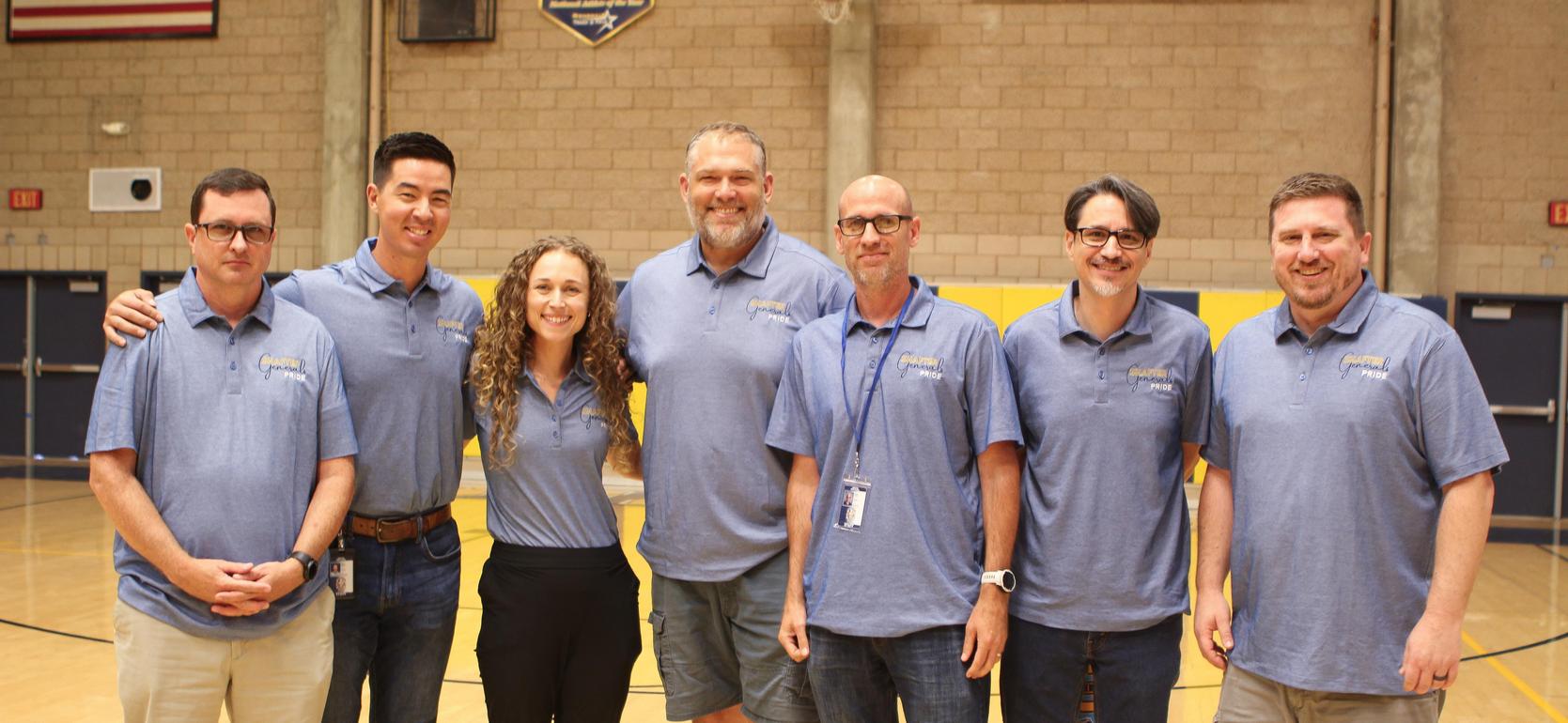 Team of staff members in blue shirts standing on a gym floor.