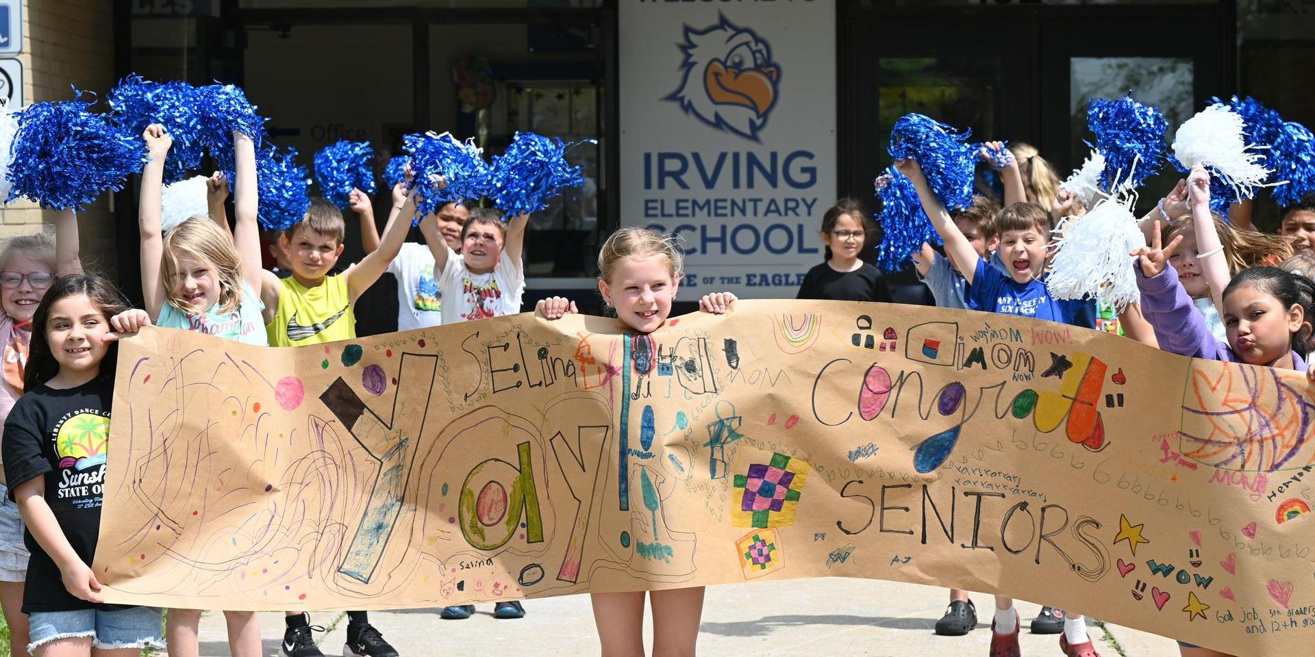 Students celebrating with pom-poms and a banner outside their school.