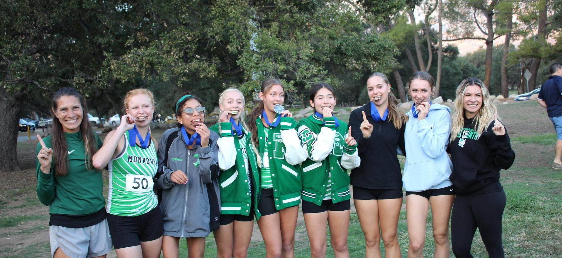 A group of eight female runners wearing medals, smiling and posing together outdoors.