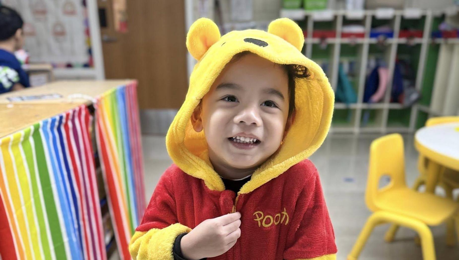 Child wearing a Winnie the Pooh costume, smiling happily in a bright room.