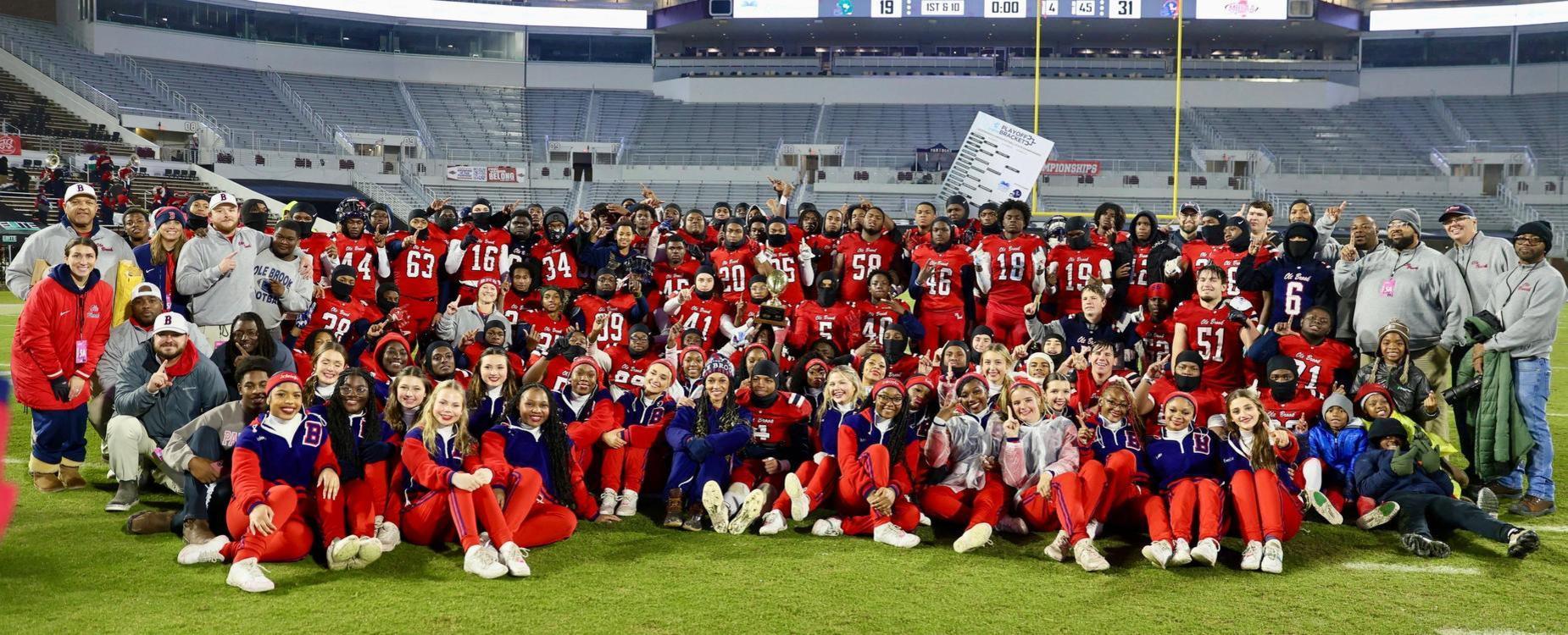 A large group of football players and supporters posing together on the field after a game.