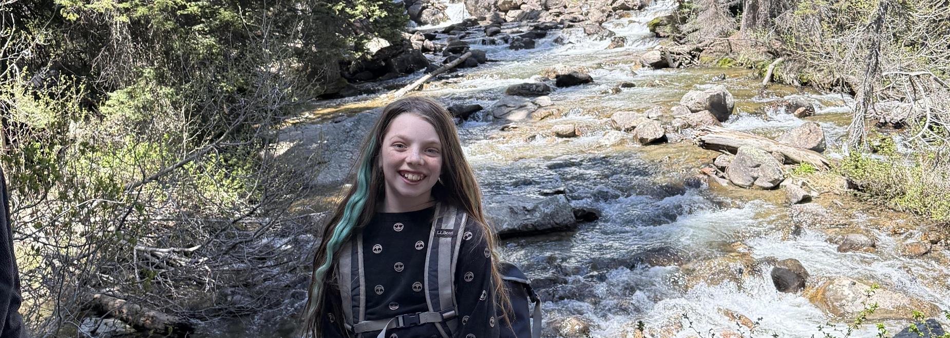 Person with long hair smiles in front of a waterfall and river.