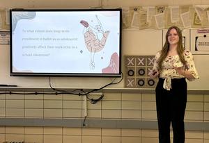 A young woman explains how ballet enrollment impacts classroom work ethic, shown on a screen.