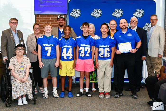 A group of football players and a coach smiling with school board members, holding an award