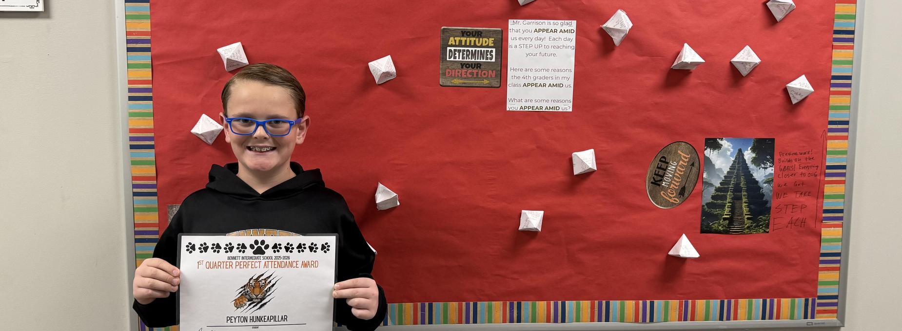 Boy posing with a certificate in front of a colorful, motivational wall.