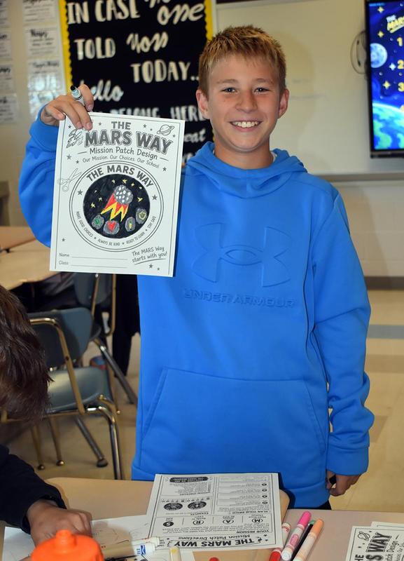 Smiling boy holding up a colorful mission patch design.