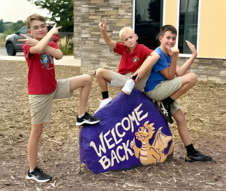 Three elementary school kids posing around a decorated spirit rock