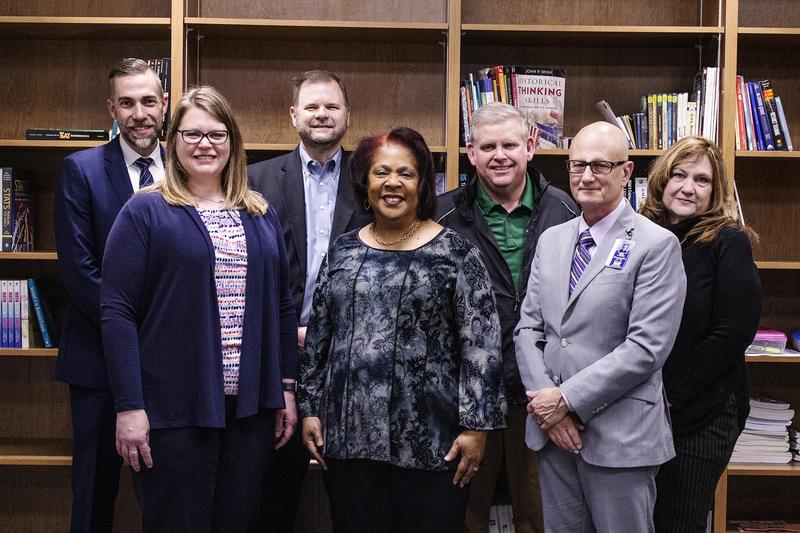 7 administrators pose together in front of a bookcase