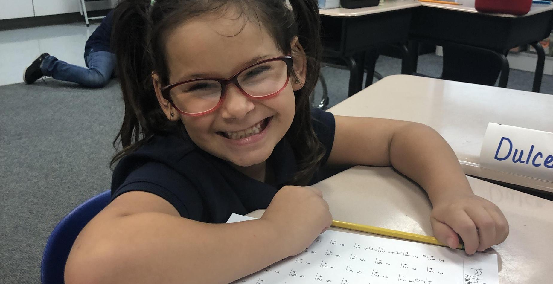 a second grade girl smiling as she completes her math assignment