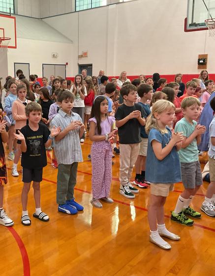 A diverse group of children gathered in a gym, some clapping and interacting.