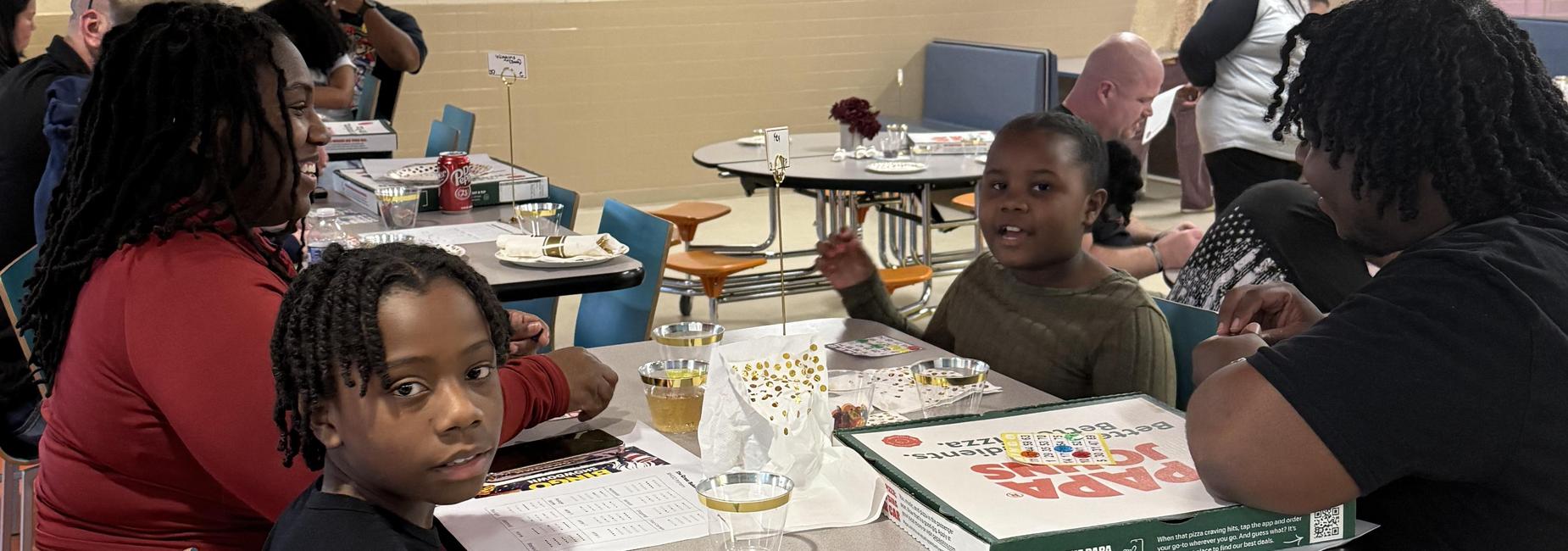 A family enjoying a meal together at a table with pizza and drinks.