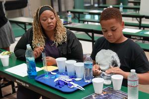 A woman watches as a boy uses a spoon to measure