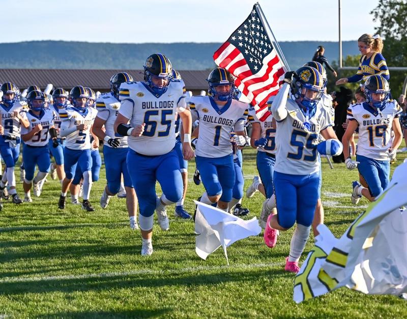 Claysburg Kimmel football team running onto the field with an American Flag