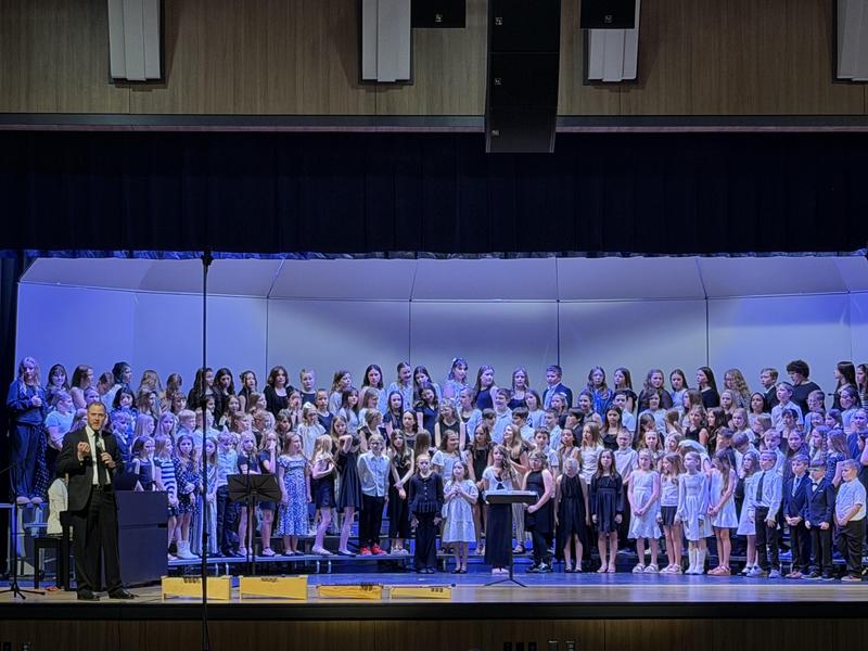 students performing in auditorium with director speaking at microphone