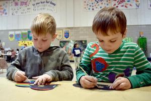 Two boys focused on crafting at a table, surrounded by a vibrant classroom atmosphere.