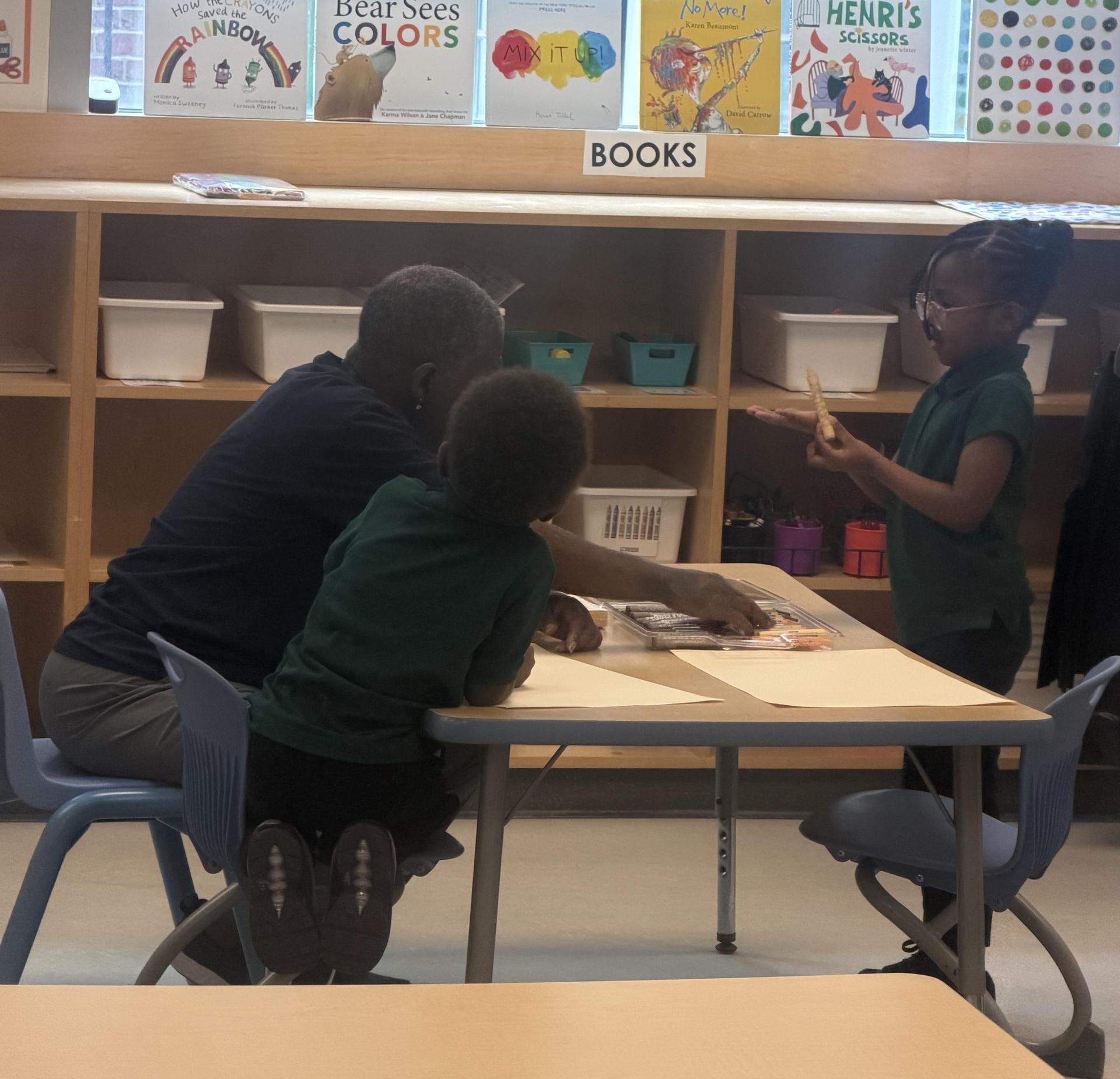 An adult and two children engage at a table in a classroom.