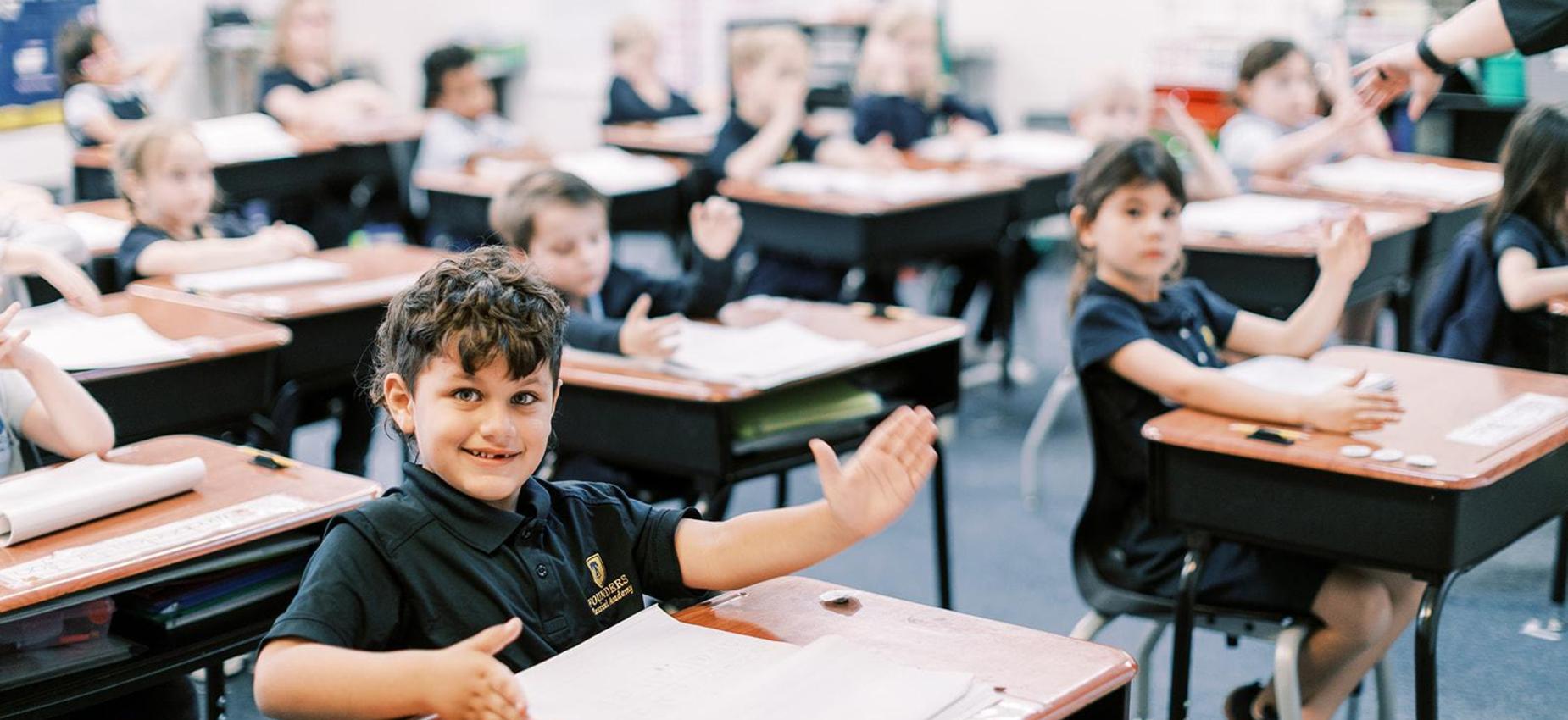 Smiling elementary student gestures from his desk during class