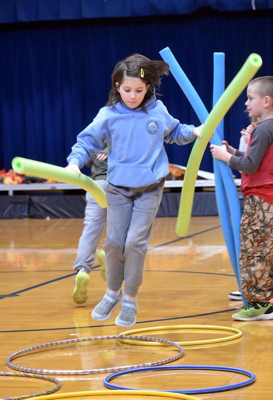 a student holding pool noodles and jumping over hula hoops